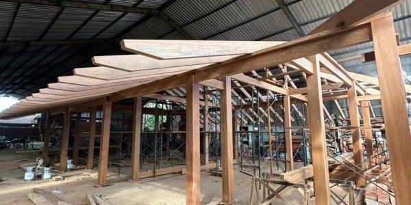 Timber structure of a Kontiki-style building under construction inside a warehouse, featuring solid hardwood columns and beams with exposed rafters