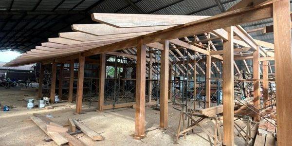 Kontiki building prototype in progress, showcasing hardwood framing and roof rafters within a large covered workshop