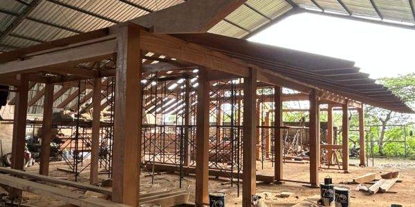 Wide shot of a hardwood Kontiki structure being assembled in a warehouse, with beams, planks, and construction tools placed around the workspace