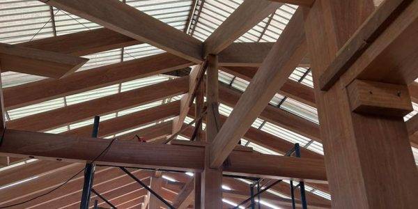 close up of a hardwood Kontiki structure being assembled in a warehouse, with beams, planks, and construction tools placed around the workspace
